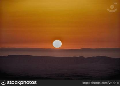 Sunrise over the Maktesh Ramon Crater the morning after a sandstorm results in a bright orange glow in the sky.