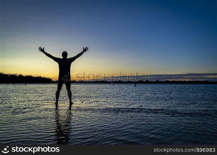sunrise silhouette of a man standing in shallow water and stretching or practicing chigong movements, Boyd Lake State Park in northern Colorado