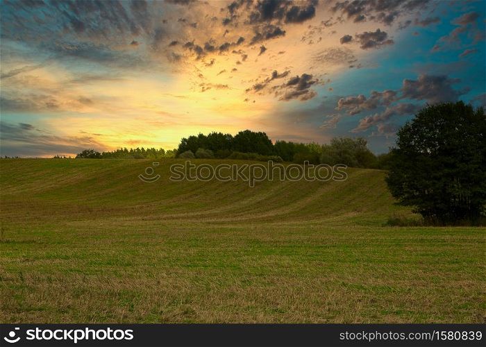 Sunrise with beautifully lit clouds. Meadows, fields and forest in summer. Poland.Horizontal view.