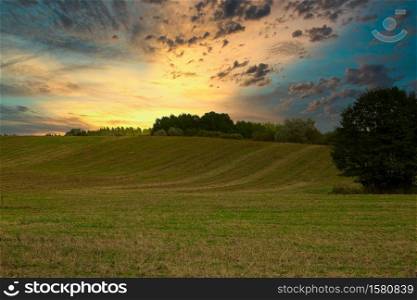 Sunrise with beautifully lit clouds. Meadows, fields and forest in summer. Poland.Horizontal view.