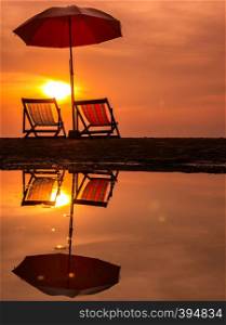 Sunrise with orange morning sky over sea with chair and umbrella on beach reflection in water, Thailand