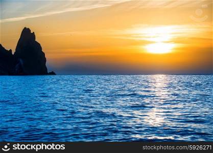 Sunset above blue sea with rocks and orange sky