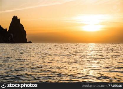 Sunset above the sea with rocks and orange sky