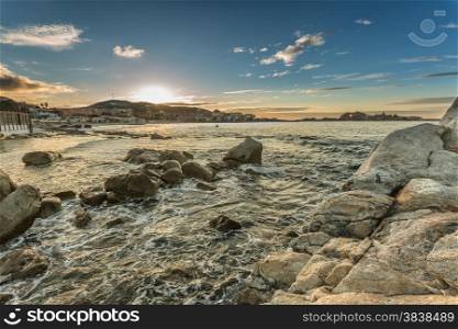 Sunset and clear skies over the town of Ile Rousse on the west coast of the Balagne region of Corsica with rocks and mediterranean sea in foreground and lights coming on in the town.
