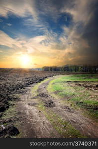 Sunset and country road through the plowed field