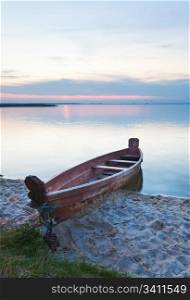 Sunset and old wooden fishing boat near the summer lake shore (Svityaz, Ukraine)