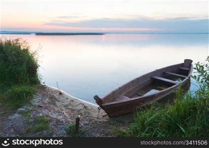 Sunset and old wooden flooding boat near the summer lake shore (Svityaz, Ukraine)