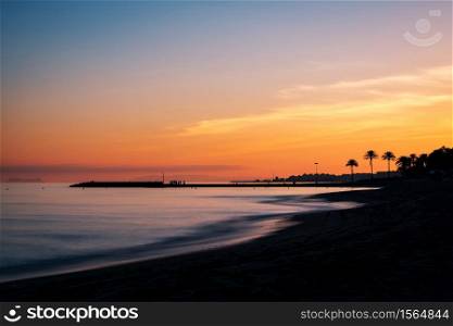 Sunset at a beach in the Costa del Sol in Marbella, Spain, with the silhouette of a pier and Gibraltar to be recognised in the background. Long exposure.