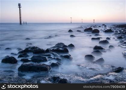 Sunset at beach with boulders and masts in the water