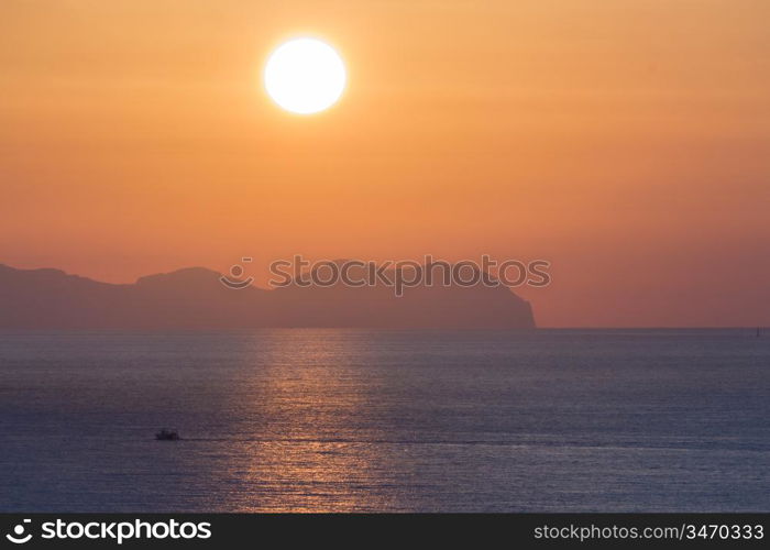 Sunset at sea with shipping boat silhouette.