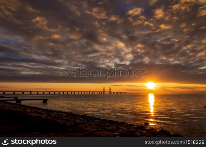 Sunset at the sea shore. Bridge over the bay. Cloudy skye
