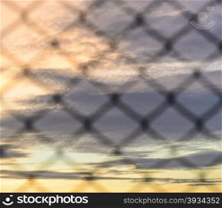 Sunset background with blurry wire mesh fence