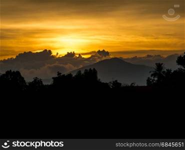 Sunset behind cloud and mountain with silhouette tree in front