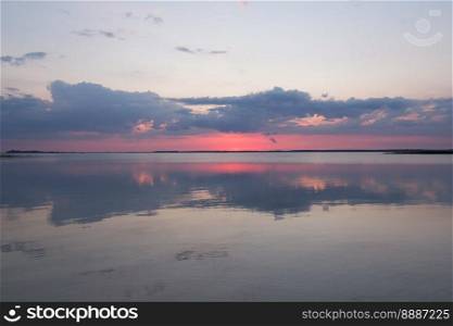 Sunset clouds reflecting on lake landscape photo. Beautiful nature scenery photography with skyline on background. Idyllic scene. High quality picture for wallpaper, travel blog, magazine, article. Sunset clouds reflecting on lake landscape photo