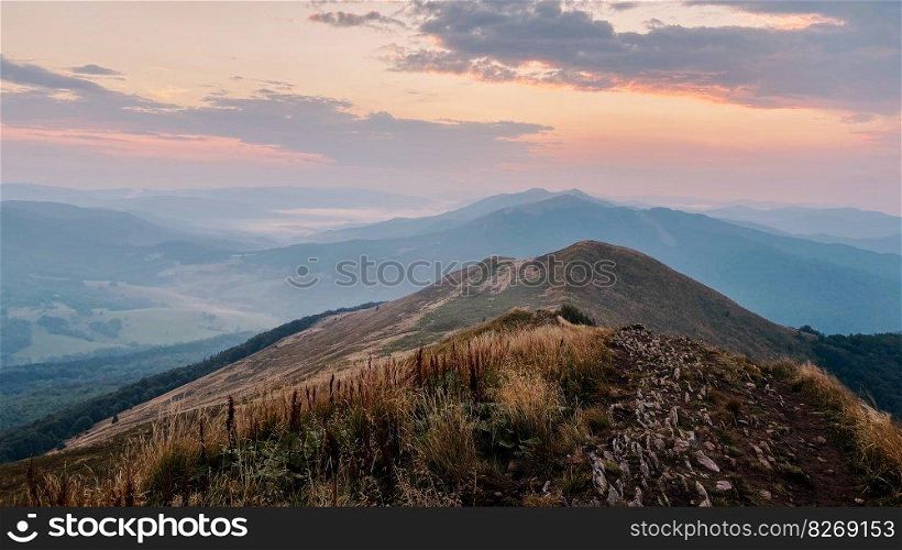 Sunset in mountains. Natural mountain landscape with illuminated misty peaks, foggy slopes and valleys, blue sky with orange yellow sunlight. Amazing scene from Bieszczady Mountains in Poland