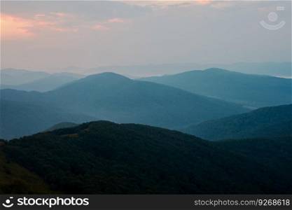 Sunset in mountains. Natural mountain landscape with illuminated misty peaks, foggy slopes and valleys, blue sky with orange yellow sunlight. Amazing scene from Bieszczady Mountains in Poland