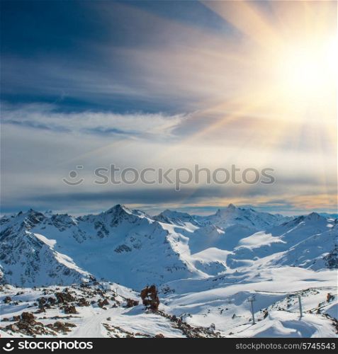 Sunset in snowy blue mountains with clouds. Winter ski resort