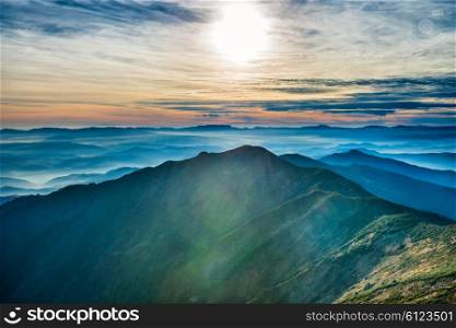 Sunset in the mountains. Sun and colorful clouds over blue hills
