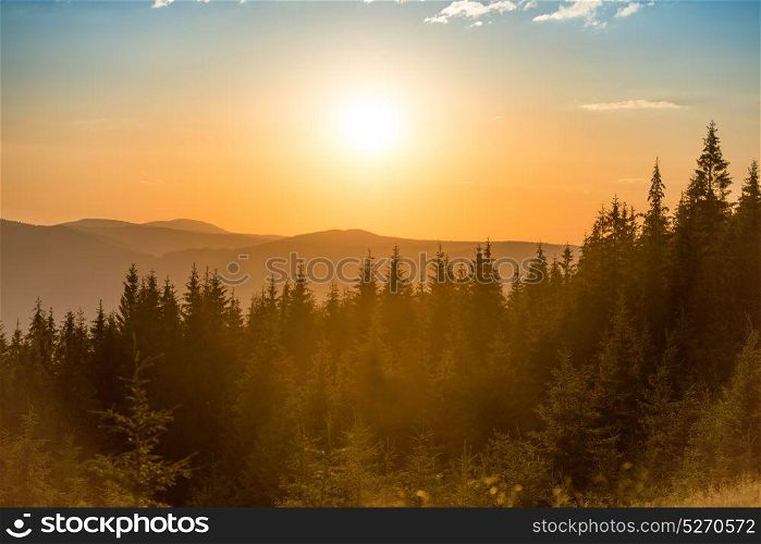 Sunset in the mountains with forest and big shining sun on dramatic sky
