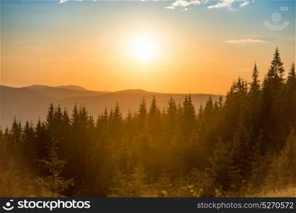 Sunset in the mountains with forest and big shining sun on dramatic sky
