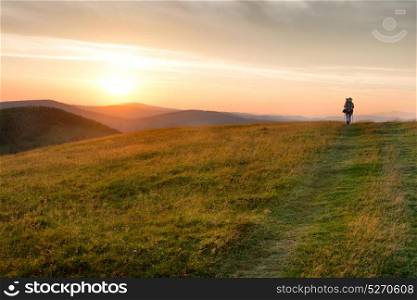 Sunset in the mountains with woman silhouette, green grass and big shining sun on dramatic sky