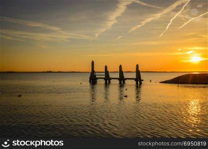 sunset in the northsea with lines from planes in the sky and wooden structure in the water. sunset in the northsea