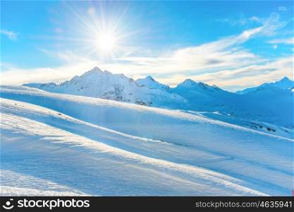 Sunset in winter mountains covered by snow. Shining sun on the blue sky