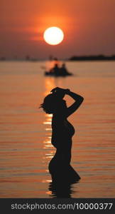 Sunset ocean view. Sun above the sea on orange sky. Woman standing on beach.