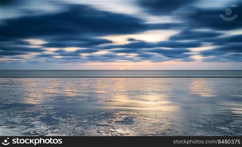 Sunset of the sea with clouds in the background. Beach and sea water with long exposure.. Beach at sunset (mud flat ) me passing clouds at Waddenzee