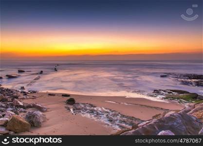 sunset on a beach with gold sand and rocks in portugal