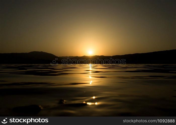 Sunset on a lake shore. Sun light reflections on water surface.