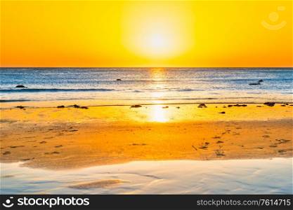 Sunset on beautiful sand beach with blue sea water and sun on sunset sky