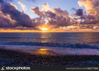 Sunset on the beach on the Black Sea coast in Sochi. Sea waves breaking on a stony beach