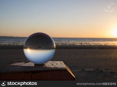 sunset on the beach on wooden pole captured in glass crystal sphere