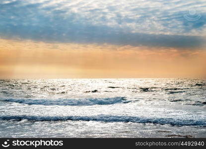 Sunset on the blue sea with waves and dramatic clouds