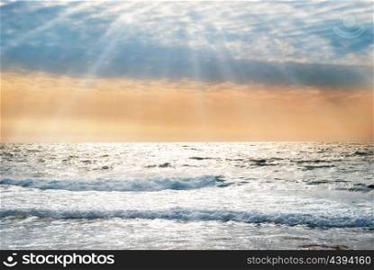 Sunset on the blue sea with waves and dramatic clouds and sun rays
