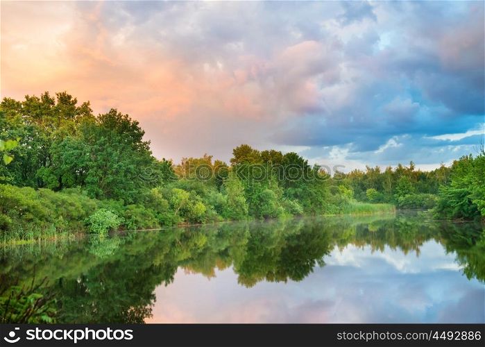 Sunset on the lake with green forest and colorful sky