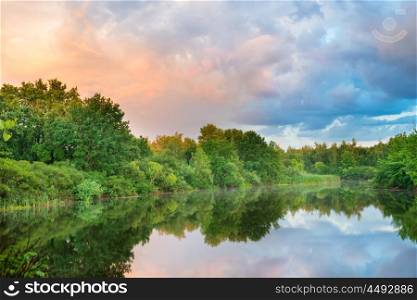 Sunset on the lake with green forest and colorful sky
