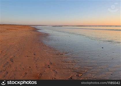 sunset on wet sand at low tide with footsprint