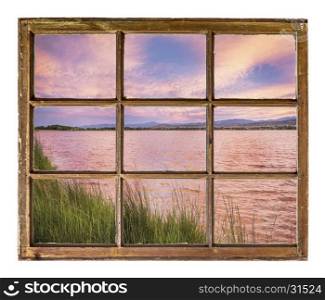 sunset over a lake with Rocky Mountains in background as seen from a sash window of an old cabin