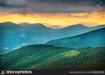 Sunset over blue mountains. Green forest on background