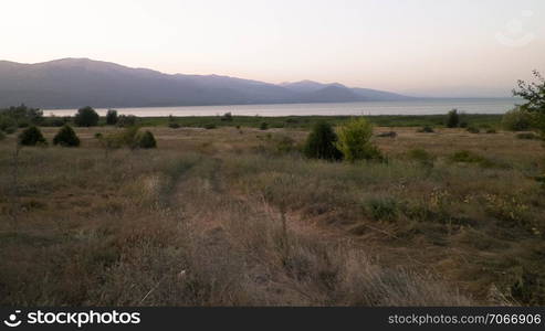 Sunset over coast of Lake Prespa and Mountains of Galicica National Park, Macedonia. Galicica is National park between two lakes - Ochrid and Prespa, known of it&rsquo;s wild nature. Balkan nature and exploration concept.. Sunset over coast of Lake Prespa and Mountains of Galicica National Park, Macedonia