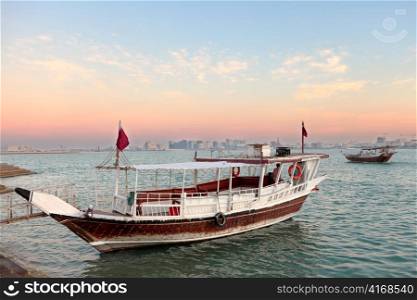 Sunset over Doha Bay, Qatar, Nov 20, 2011, with two of the excursion dhows that take visitors on short sightseeing trips along the shore. Various landmark buildings are visible on the distant skyline.