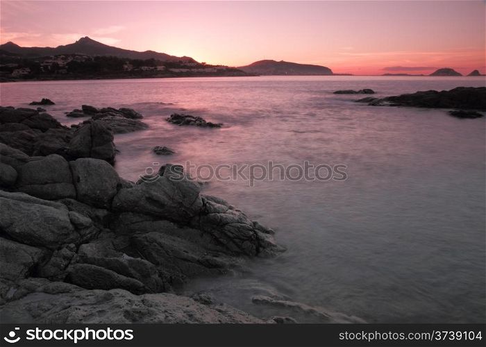 Sunset over Ile Rousse in Corsica. Pink sunset over Ile Rousse in the Balagne region of Corsica with rocks and the sea in the foreground