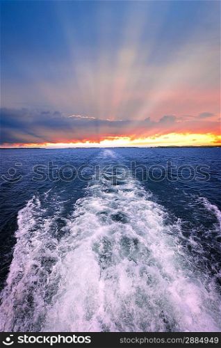 Sunset over ocean with boat wake