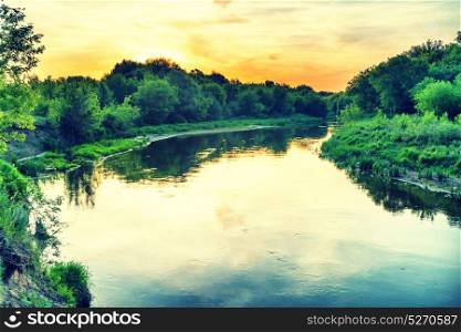 Sunset over river. Landscape with green trees, dramatic sky, clouds and sun