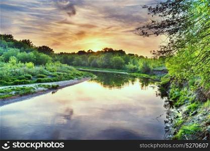 Sunset over river. Landscape with green trees, dramatic sky, clouds and sun