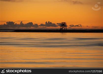 Sunset over the Baltic sea in Parnu coloring water in orange with silhouette of Vana-Parnu bird watching tower on horizon