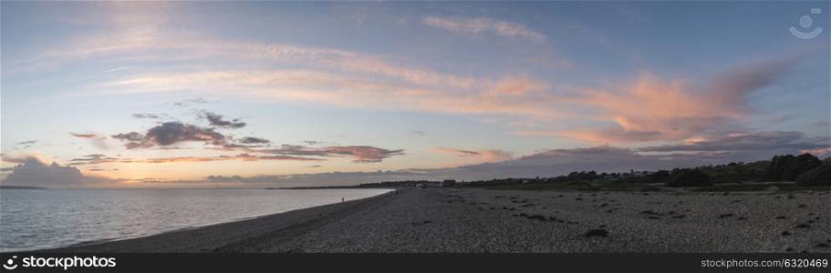 Sunset panorama over shingle beach with colorful vibrant sky