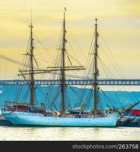 Sunset scene with sail ship in harbor by 25th April Bridge, Lisbon, Portugal